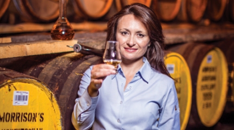 Woman holding whisky glass in front of whisky barrels